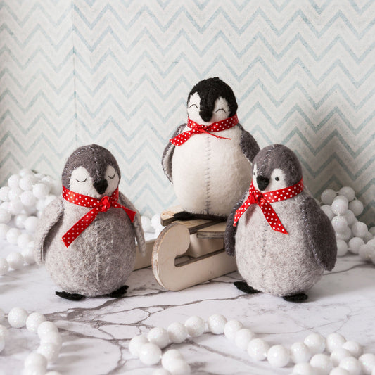 Corinne Lapierre Felt Baby Penguins Craft Kit. Snow Scene. 3 felt penguins in grey, black & white, with red ribbon tied at neck.