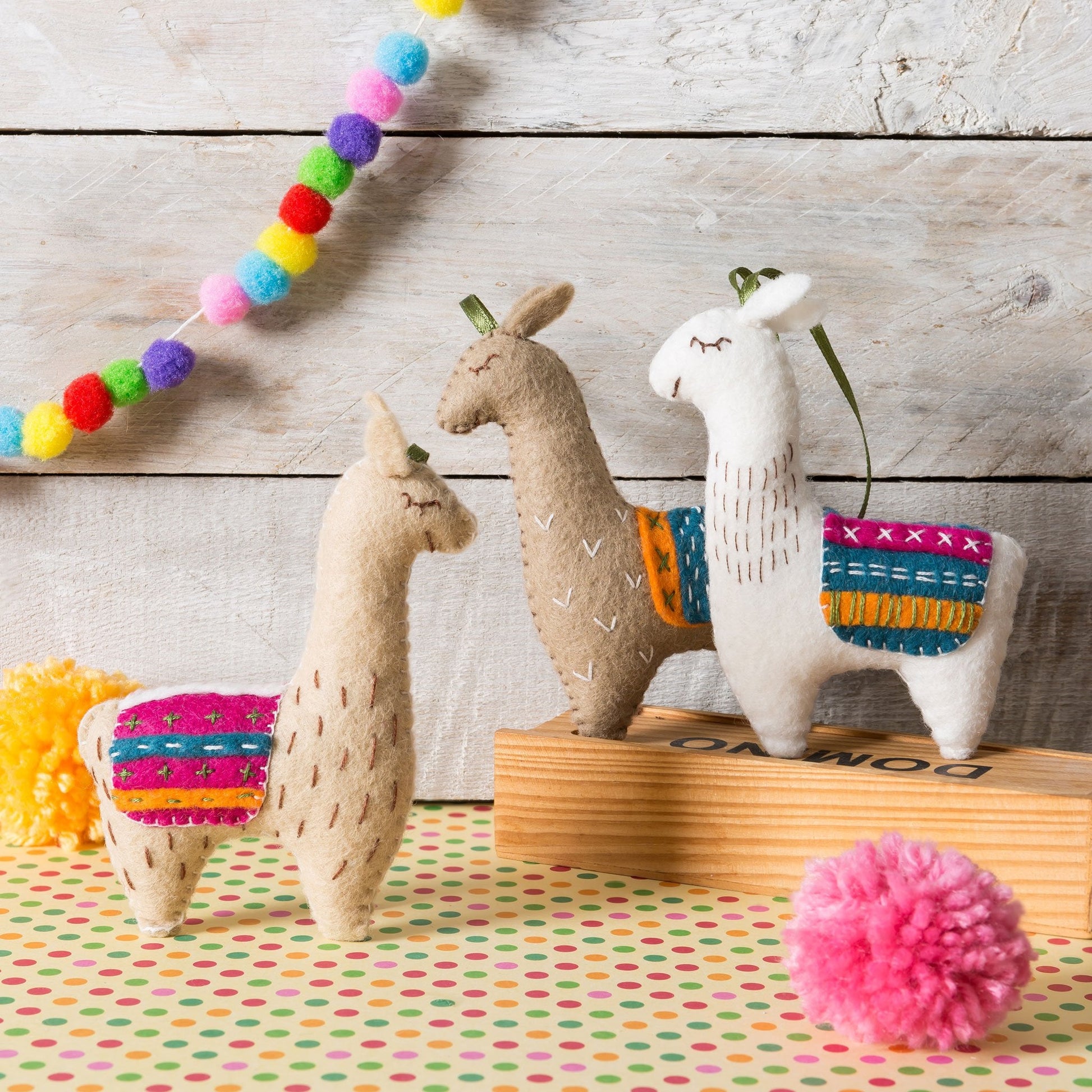 Corinne Lapierre Felt Llamas Craft Kit. A colourful scene. There are 3 Llamas. All three Llamas are wearing multi coloured waistcoats. 